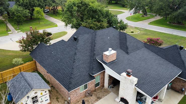 Aerial view of a house with a dark shingle hip roof in a suburban neighborhood