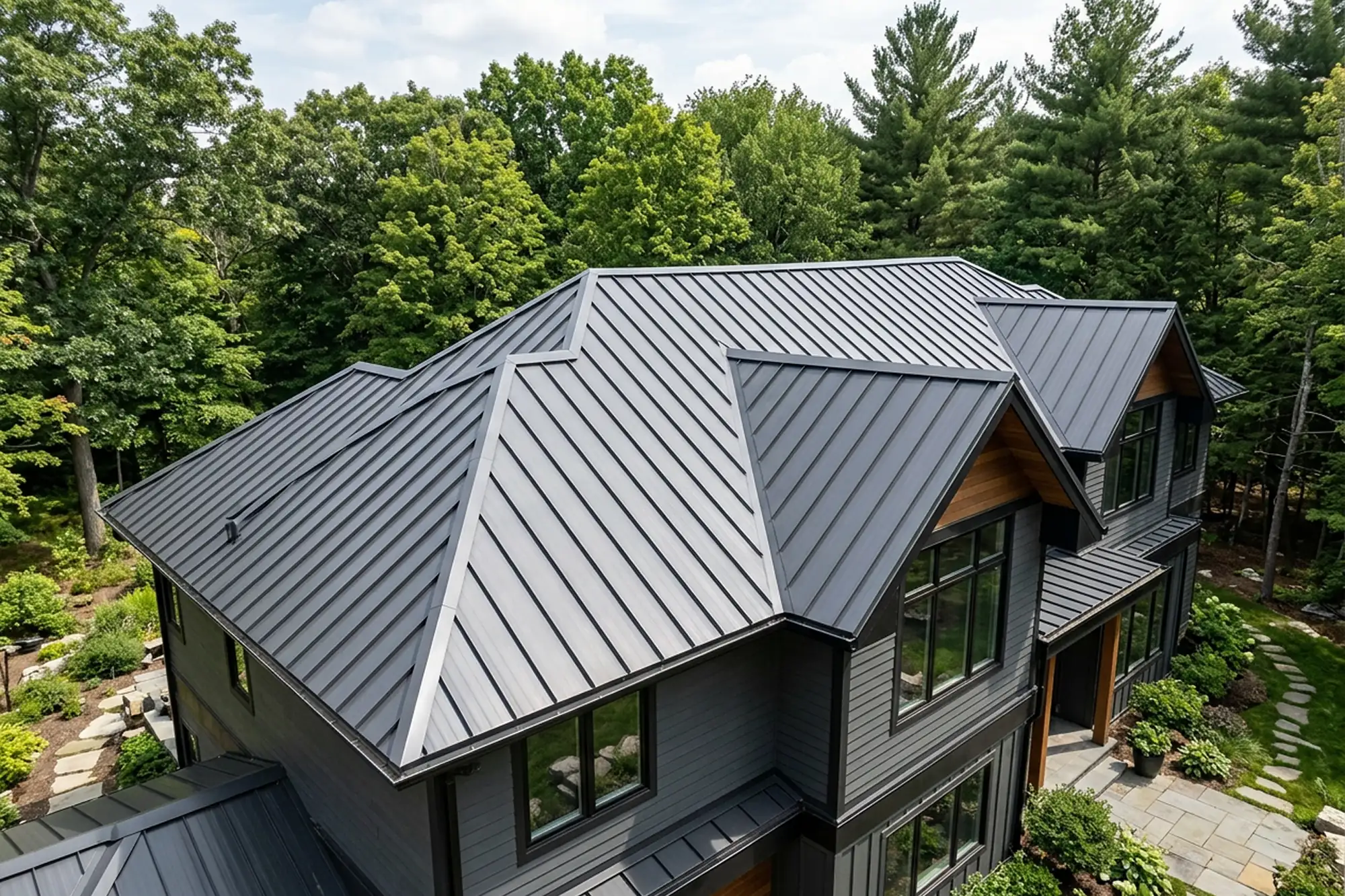 Aerial view of a modern home with a grey standing seam metal roof surrounded by trees